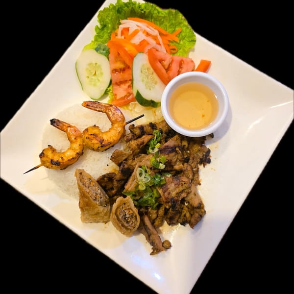 A Vietnamese dish with grilled shrimp, sliced beef, rice, spring rolls, salad, and dipping sauce.