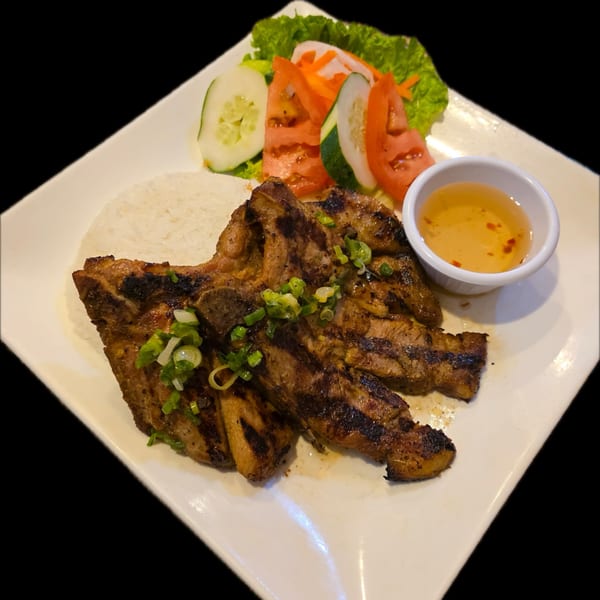 Grilled pork chops with rice, a side salad of lettuce, cucumber, tomato, and a small bowl of sauce.
