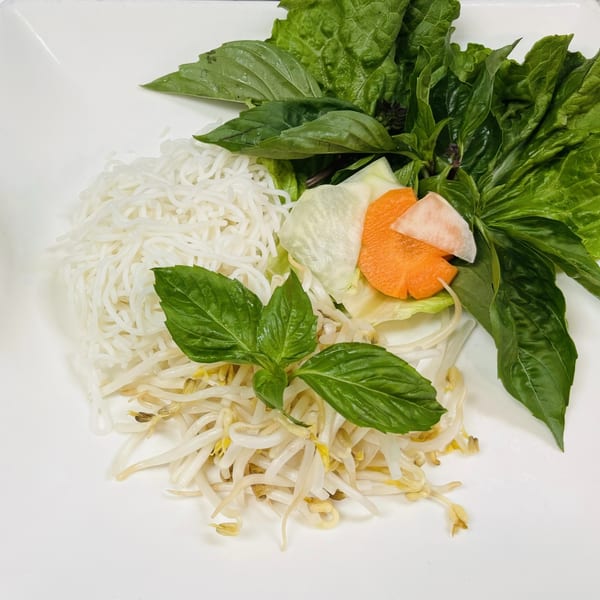 Fresh Vietnamese pho garnishes including basil, bean sprouts, rice noodles, and pickled vegetables.