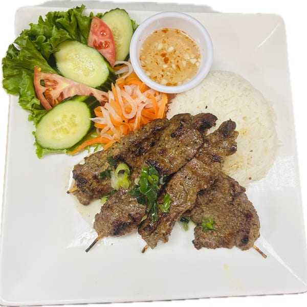 Grilled beef skewers with rice, a side salad, pickled vegetables, and dipping sauce.