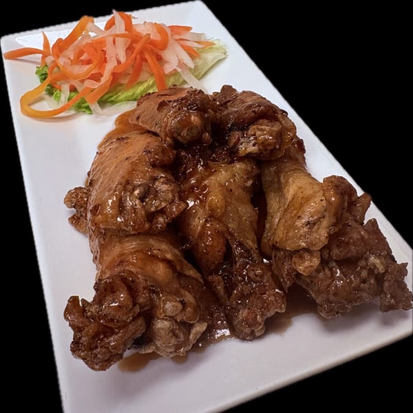 Vietnamese chicken wings with a glossy sauce, served with pickled carrots and daikon on a white plate.