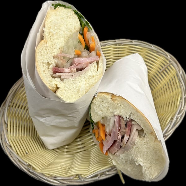 Two Vietnamese banh mi sandwiches, wrapped in paper, filled with meat and vegetables, in a wicker basket.